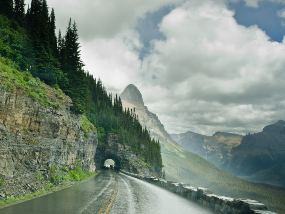 A damp road leading to a small tunnel with pine trees overhead at Going-to-the-Sun Road, driving by this scenic mountain road is one of the best things to do in Montana